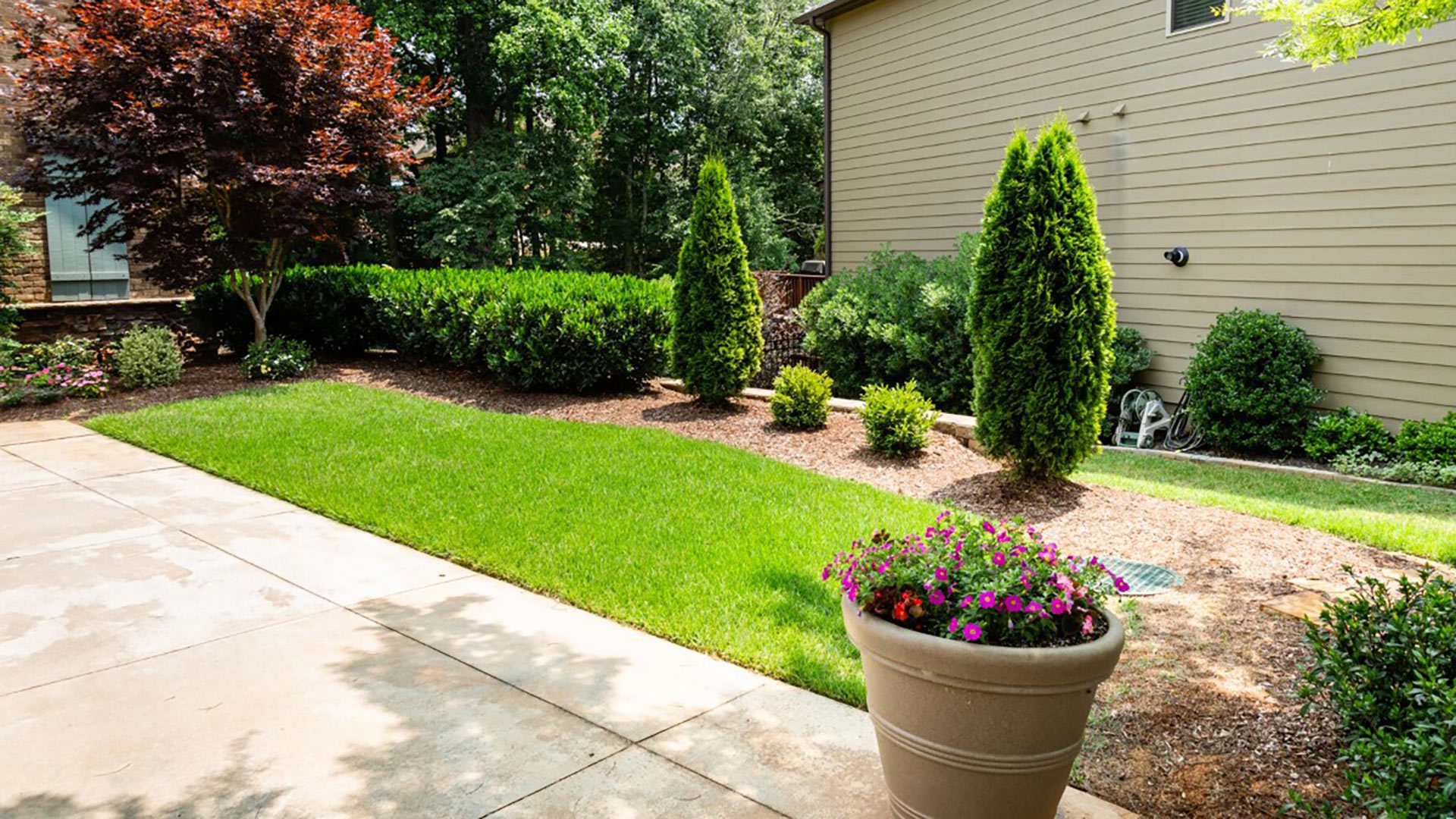 A landscape bed of bushes and shrubs with a pot of flowers in West Chester, PA.