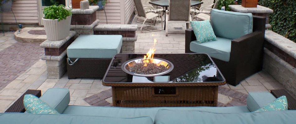 An outdoor fire table on a paved stone patio surrounded by furniture in Chester Springs, PA.