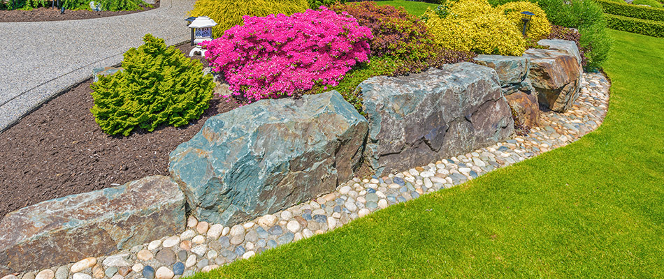 A retaining wall made of rocks around a bed of bushes and flowers in Malvern, PA.